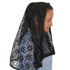 Person wearing a black lace headscarf against a plain wall
