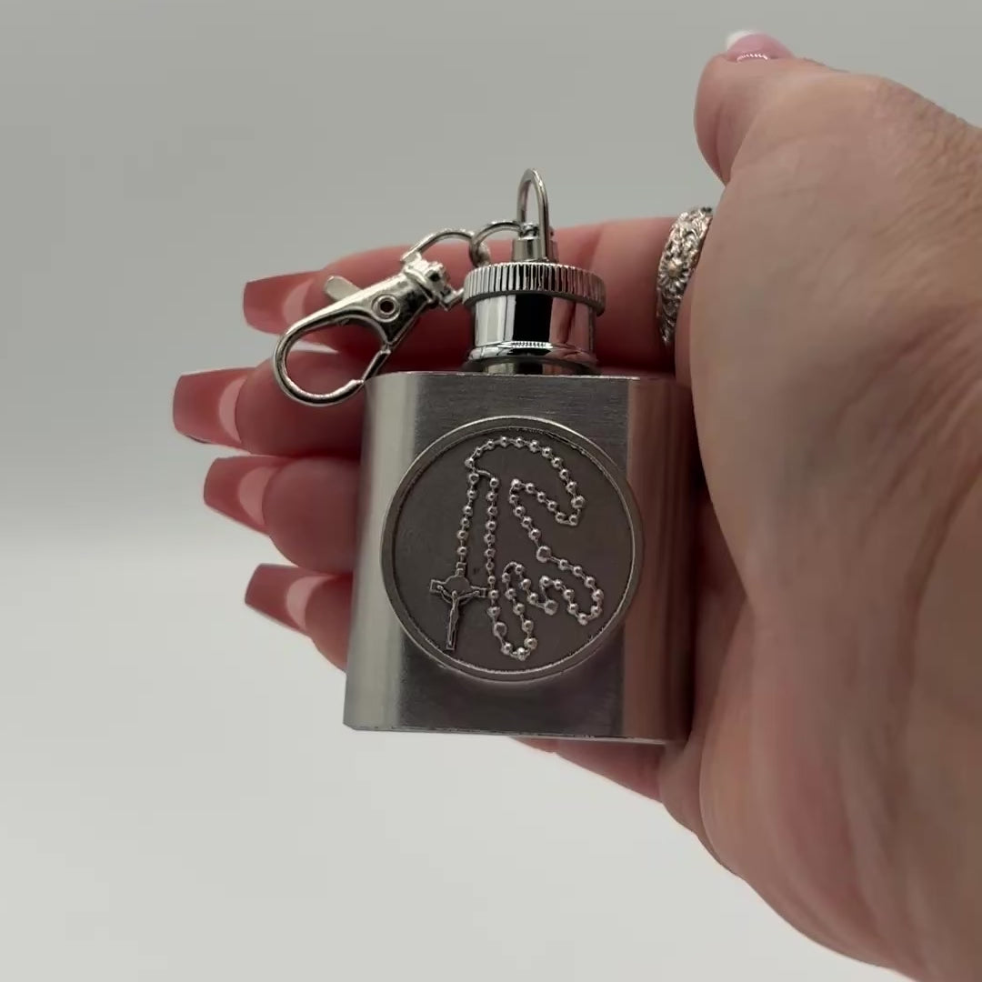 video of a ladies hand displaying a small square stainless steel holy water flask. Turning the product, allowing you to see many angles.